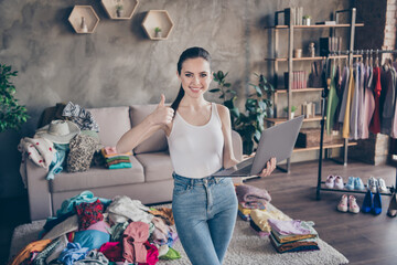 Portrait of positive girl use laptop approve online purchase buying fabric clothes enjoy show thumb-up sign stand in house indoors