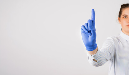 Cropped view of young female in a white shirt and in blue sterile gloves shows a sign with finger attention on white background.