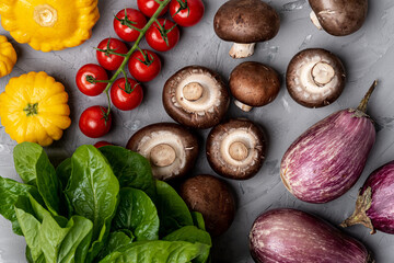 
Healthy vegetable composition. Eggplants, squash, tomatoes, mushrooms and spinach on a gray surface. Top view.