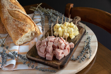 Rustic cutting board arrangement with mortadella and Italian cheese with toothpick, with bread on wooden cutting board and lavender sprigs. Typical Italian aperitivo food.