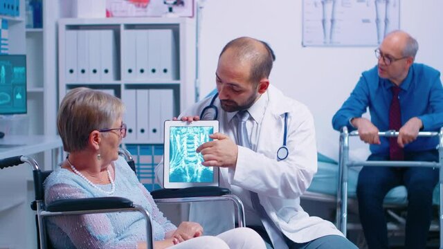 Doctor showing brain X ray image to elderly senior woman in a wheelchair, in a recovery clinic or hospital. Modern health care treatment, rehabilitation program for invalids and handicapped persons