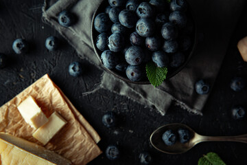 Group of organic blueberries with fresh mint leaves, next to homemade cheese, on top of the dark background. 