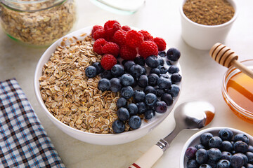 Fresh muesli breakfast on top of served kitchen table. White bowl with flakes, blueberry, raspberry, honey and milk. 