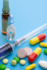  Colored tablets, syringe for injection and ampoules with the drug. Pharmaceutical industry. Blue background, studio shot.