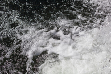White foamed surface of the water at the foot of the waterfall. Air bubbles in the water.