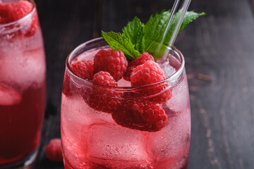 Fresh ice cold berry juice drink with mint, summer raspberry lemonade in glass with straws on dark wooden background, angle view macro