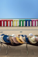 Straw hats for sale in front of multi-colored beach huts in Dunkirk, France.