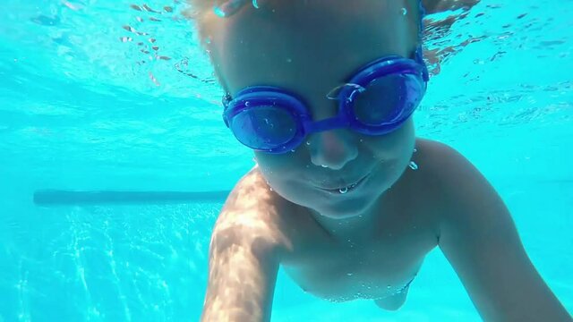 Young boy in swimming goggles jumps underwater into a pool