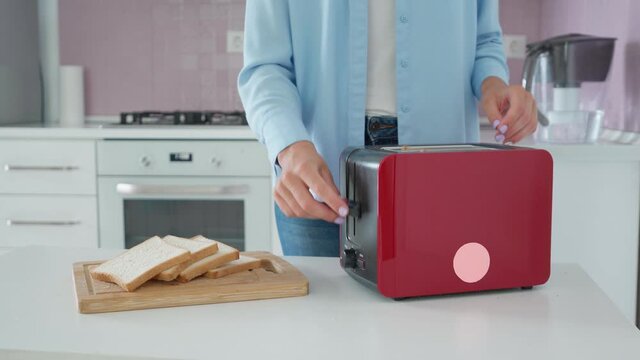 Woman using red electric toaster for making crunchy roasted toast bread for snack 