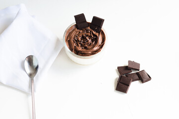 White dessert with chocolate mousse in the glass jar, pieces of chocolate on the white background