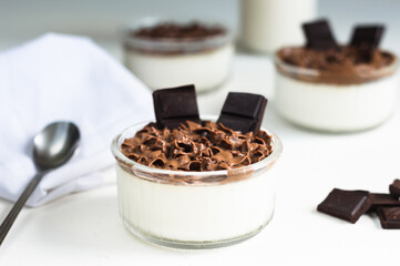 White dessert with chocolate mousse in the glass jars, pieces of chocolate on the white background