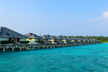 Fototapeta na wymiar Sunny beach with white sand, coconut palm trees and turquoise sea. Summer vacation and tropical beach concept. Overwater at Maldive Island resort.