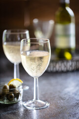 2 glasses of chilled sparkling white wine with dish of olives and sliced lemon.  Drinks tray with wine bottle and glass in background