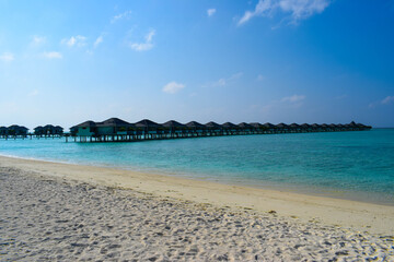 Sunny beach with white sand, coconut palm trees and turquoise sea. Summer vacation and tropical beach concept. Overwater at Maldive Island resort.