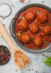Meatballs in tomato sauce with pepper, garlic and parsley on light table with utensils