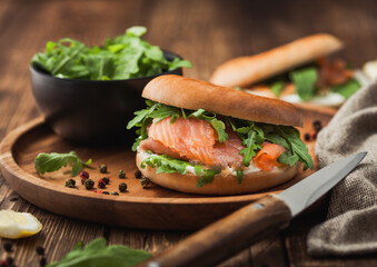 Fresh healthy organic sandwich with salmon and bagel, cream cheese and wild rocket in wooden plate with knife and linen towel.