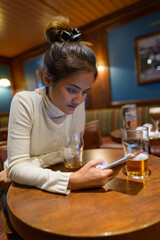 Young beautiful Asian tourist woman using mobile phone at restaurant with two glasses of beer