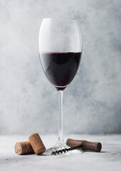 Glass of red wine with corks and opener on light background.