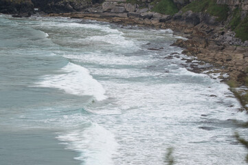 Rocky formations on the coast of Northern Ireland. Tall grassy cliffs are hit by several waves