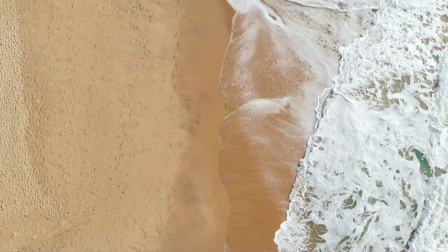 Top-down Aerial shot of green waves crashing at an empty beach shore shot with a drone in 4k.