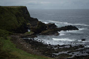 Fototapeta na wymiar Rocky formations on the coast of Northern Ireland. Tall grassy cliffs are hit by several waves