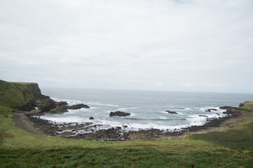 Fototapeta na wymiar Rocky formations on the coast of Northern Ireland. Tall grassy cliffs are hit by several waves
