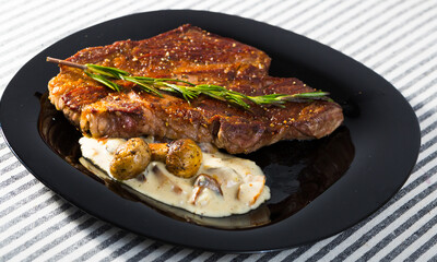 Fried beef loin decorated with rosemary served with grilled mushrooms and sauce on striped background