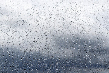Raindrops on the window glass on blurred background of sky with storm clouds. Beautiful water drops, rainy weather