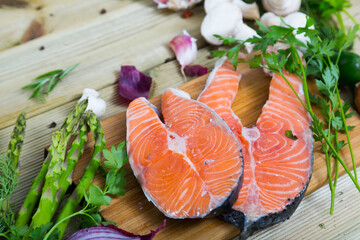 Delicious salmon steaks with fresh vegetables and mushrooms on wooden background