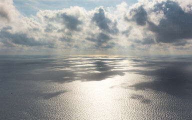 Fototapeta premium Gray beautiful clouds over the sea. Long panoramic sea autumn view. Low Cumulus clouds and bright sunlight. Shadow of clouds on the surface of the water. Gray steel natural shades of the autumn sea.