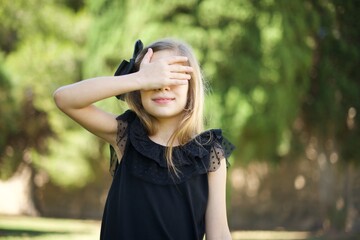 Happy Caucasian young  little girl  closing eyes with hand going to see surprise prepared by boyfriend standing and smiling in anticipation for something wonderful. Young lady covering face with hand.