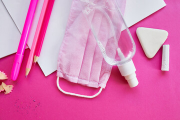 School supplies, protective mask and antiseptic on a pink background
