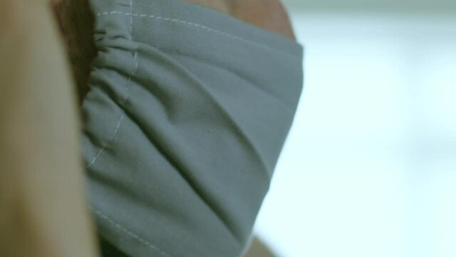 Putting on a plain grey mask close up on a male face and removing it again left of frame with slight green hue and a white blue medical bokeh