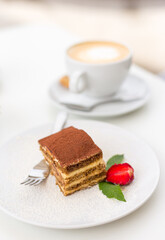 Delicious Tiramisu cake with fresh strawberries and mint on a plate on a white background. Breakfast with a Cup of coffee in cafe