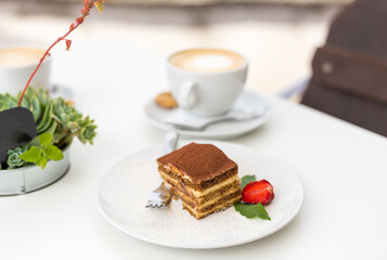 Delicious Tiramisu cake with fresh strawberries and mint on a plate on a white background. Breakfast with a Cup of coffee in cafe