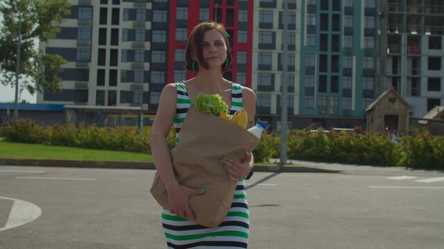 30s Woman In Dress Walking Holding Big Grocery Bag In Hands. Woman Dropping Paper Bag With Food On The Ground Accidentally. Grocery Bag Falling On The Street.