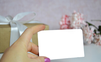 female hand holding a white card with empty card for greeting message. Valentine's Day and Mother's Day background. Holiday mock up. Top view.