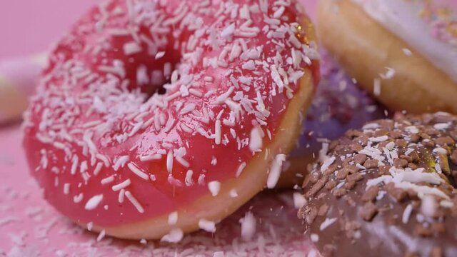 Sweet freshly baked delicious donuts with dark chololate natural flavoured frosting sprinkled with cononut flakes on pink background. Confectionery. Sweet shop.
