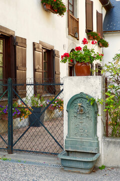 Vertical photo of entrance to the typical french house. Red colour flowers and vintage water tap in front. Saint Lary Soulan village, France