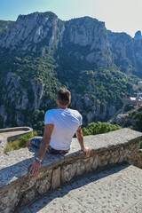 Naklejka premium Seated man looking towards the horizon, green landscape and high mountains