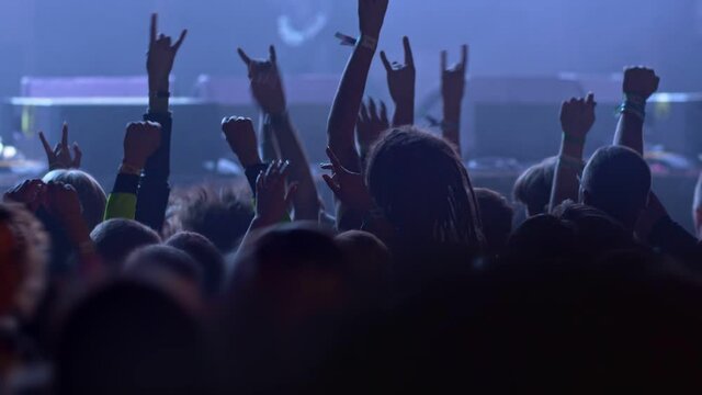 Unrecognizable fans dancing at a concert or festival party. Silhouettes of concert crowd in front of bright stage lights. slow motion
