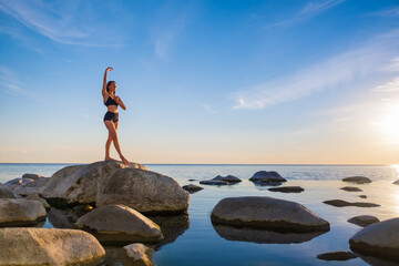 Graceful woman doing yoga on stone in evening