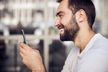 Happy young man messeges on smartphone outdoor a side view waist up portrait