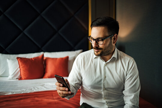 Close-up portrait of a successful businessman sitting on the bed and using smart phone.