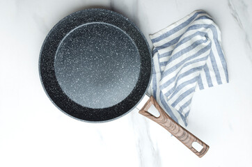 Top view of clean empty frying pan and striped napkin on the white marble table.Empty space