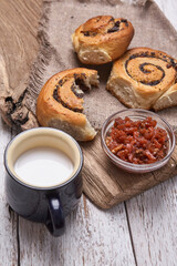 Variety of homemade puff pastry buns cinnamon served with milk cup, jam, butter as breakfast over white plank wooden background. Flat lay, space