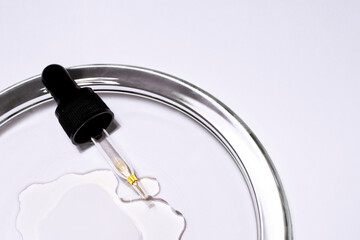 The cosmetic pipette with drops of natural liquid on a glass plate. There is space for text on a white background.