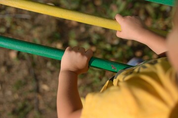 children's hands hold the horizontal bar green and yellow on the playground