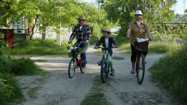 family vacations, happy male child in sun hat with their cheerful grandparents ride bicycles, during outdoor activities in country