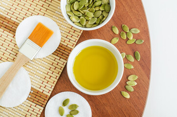 Small bowl with pumpkin seed oil, cotton pads and cosmetic brush. Ingredients for preparing homemade face or hair mask. Natural beauty treatment recipe, zero waste concept. Top view, copy space